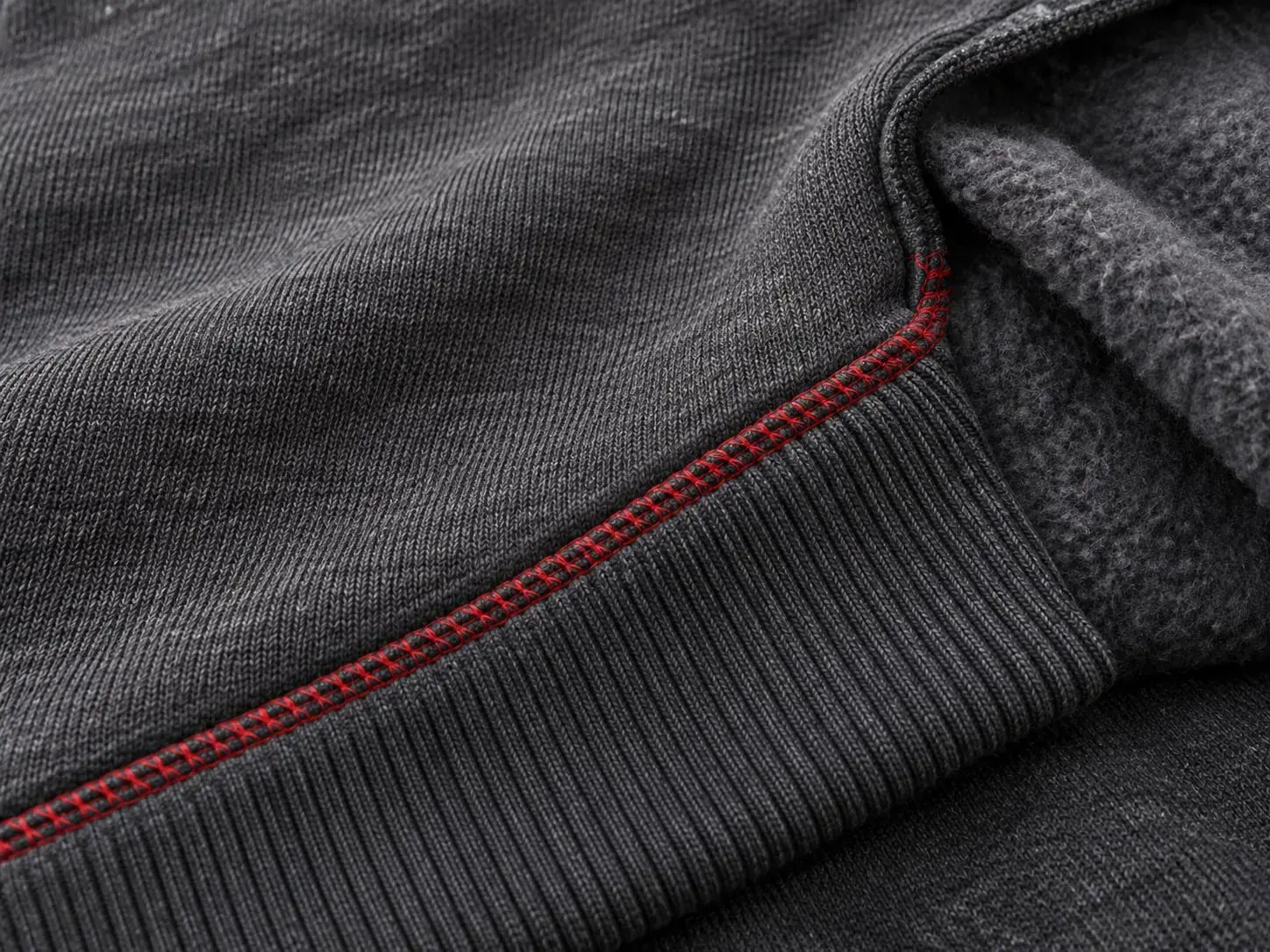 Charcoal cotton fleece with a ribbed cuff on a red overlocked seam, the brushed reverse folded back.