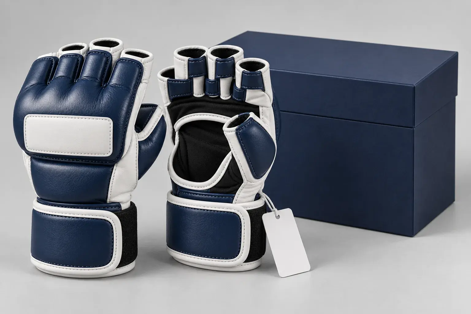 A pair of navy and white MMA sparring gloves with a blank logo panel on the back of the hand and a blank swing tag, in front of a plain navy retail box.