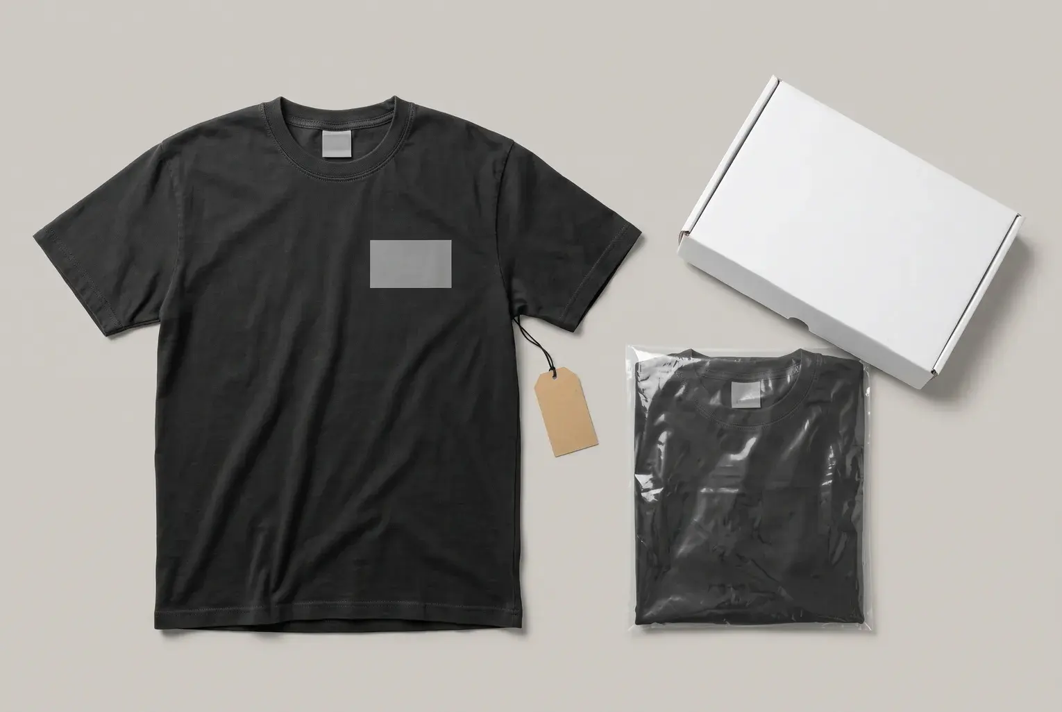 A washed black T-shirt with a blank logo panel on the chest, a blank neck label and a blank kraft swing tag, beside the same T-shirt folded in a clear polybag and a white box.