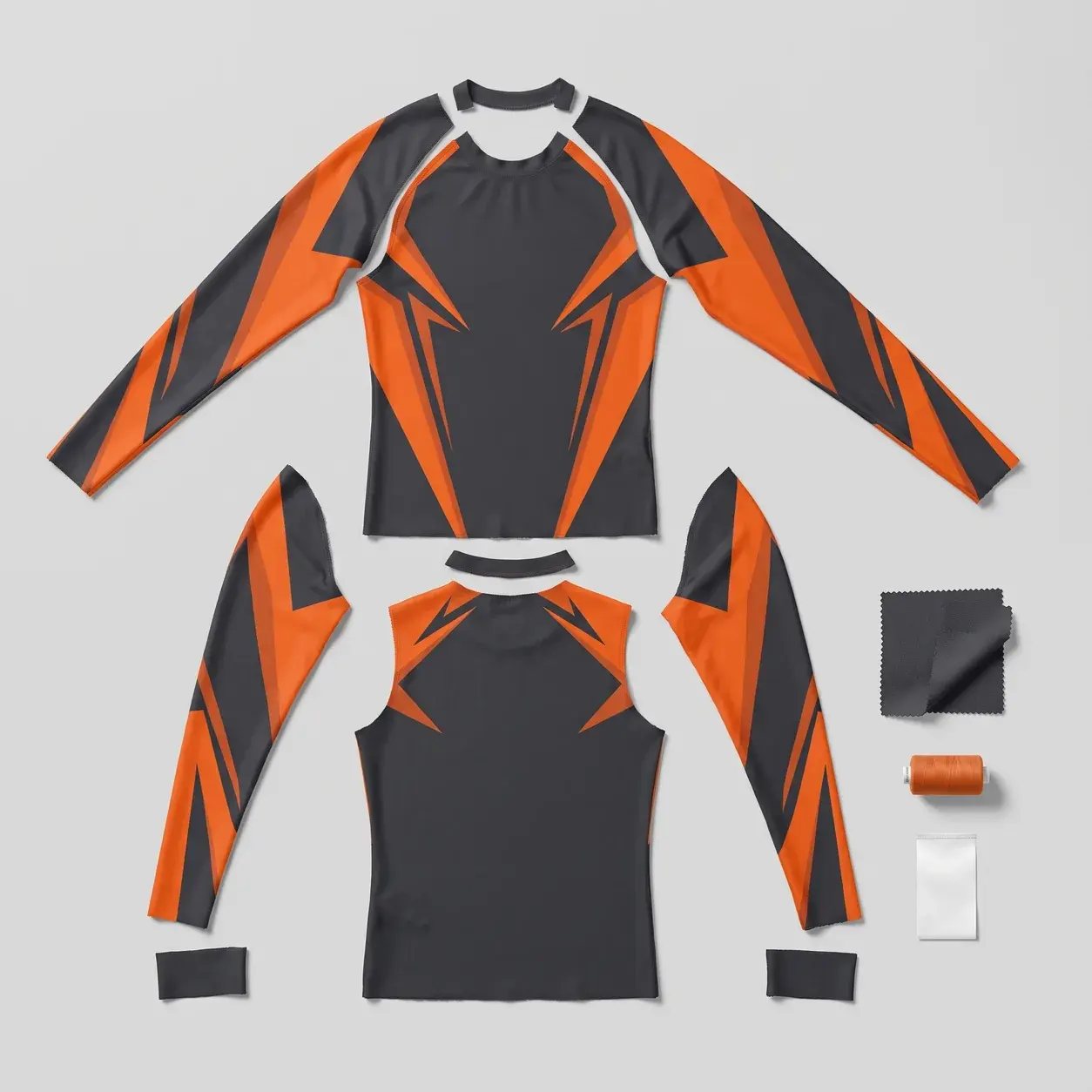A charcoal long-sleeve rash guard with orange angular sublimated panels shown in its parts: front and back panels, sleeves, neck binding and cuffs, beside a fabric swatch, orange thread and a care label.