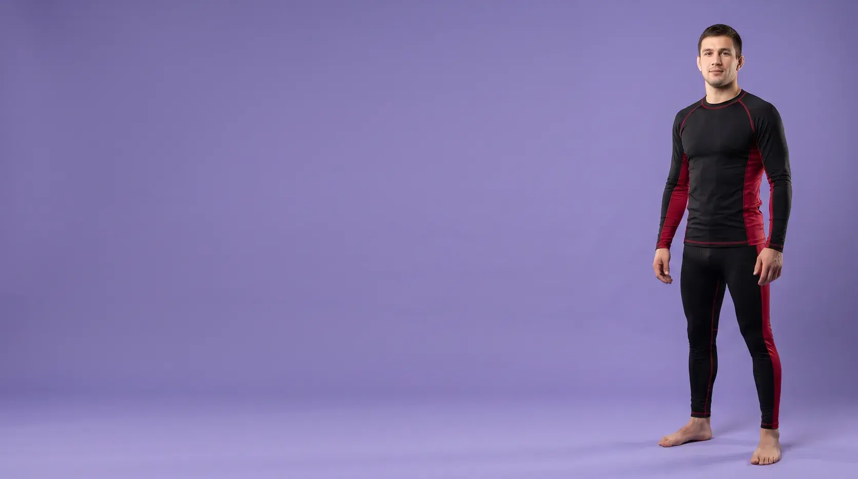 A grappler on a violet backdrop in a black long-sleeve rash guard and black spats, both with crimson side panels.