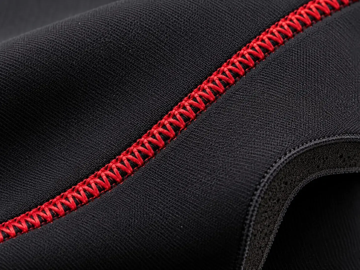 Black neoprene with a red zig-zag seam, its foam core showing at the cut edge.