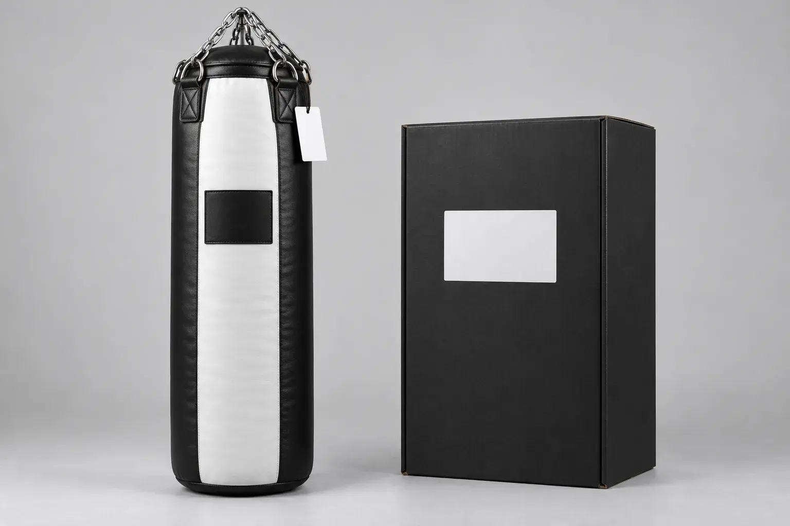 A black and white heavy bag with a blank logo panel and a blank swing tag, beside a plain black shipping carton.
